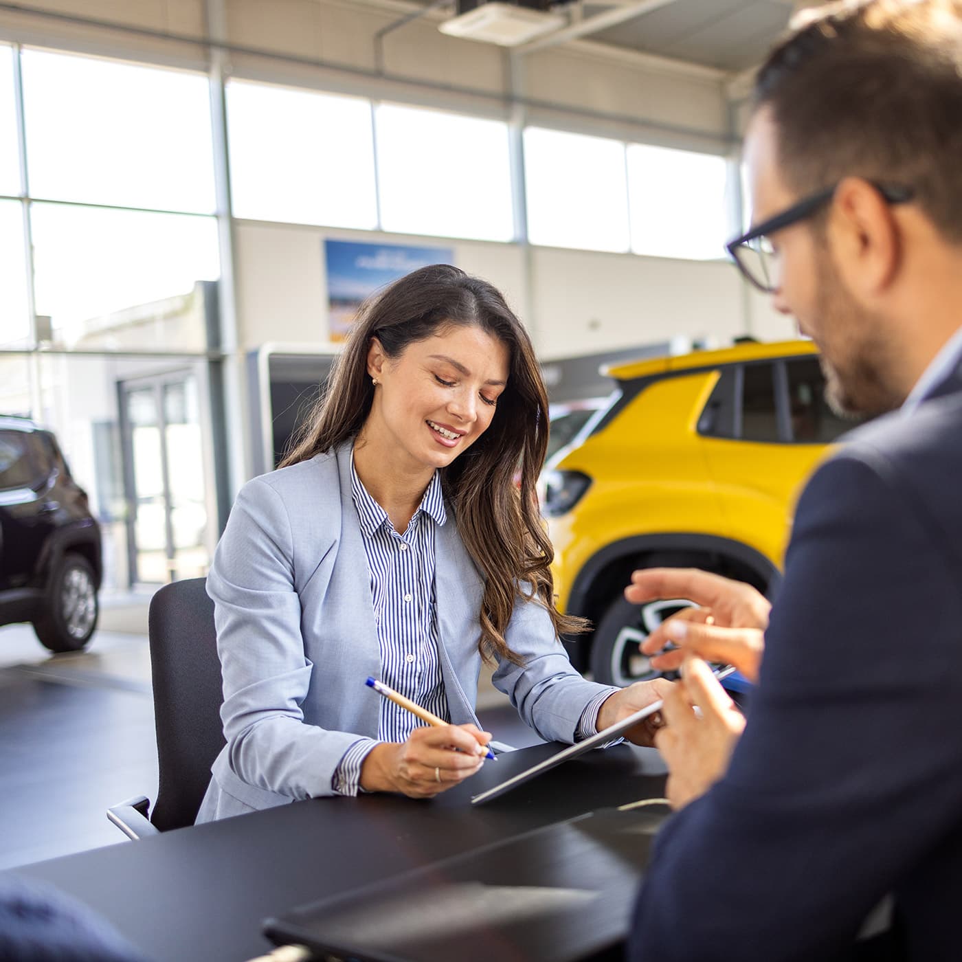 Young business woman signing car lease documents at a car dealership. Young business woman signing car lease documents at a car dealership.