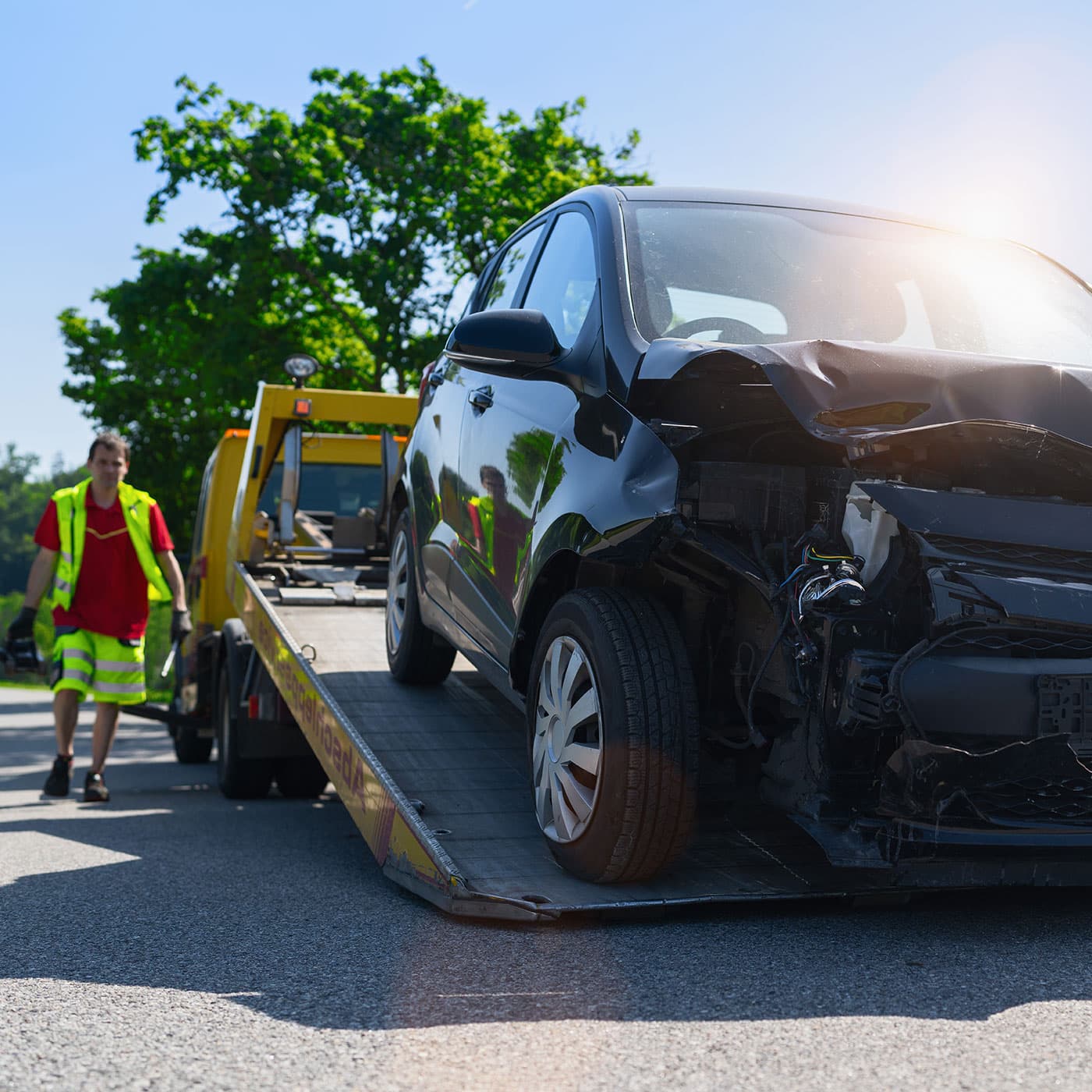 Damaged car being towed onto a flatbed tow truck with operator walking behind. Damaged car being towed onto a flatbed tow truck with operator walking behind.