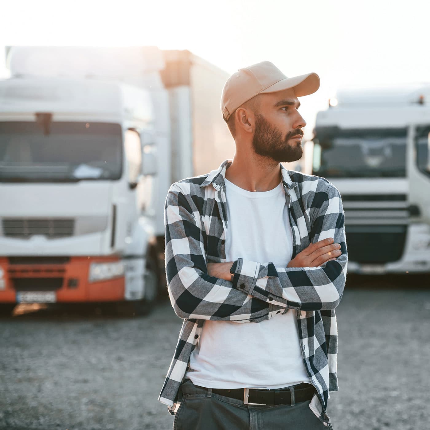 Young male truck driver wearing a baseball cap and a flannel shirt standing in front of a fleet of trucks. Young male truck driver wearing a baseball cap and a flannel shirt standing in front of a fleet of trucks.