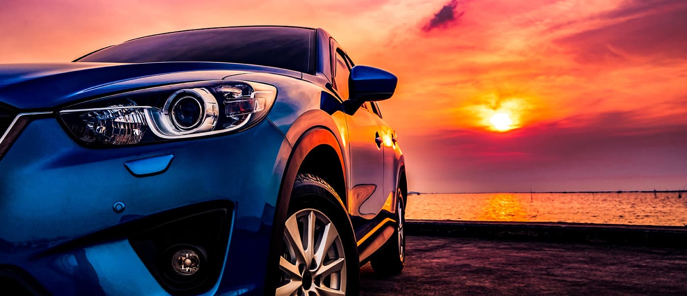 Blue compact SUV car with sport and modern design parked on concrete road by the sea at sunset. Blue compact SUV car with sport and modern design parked on concrete road by the sea at sunset.
