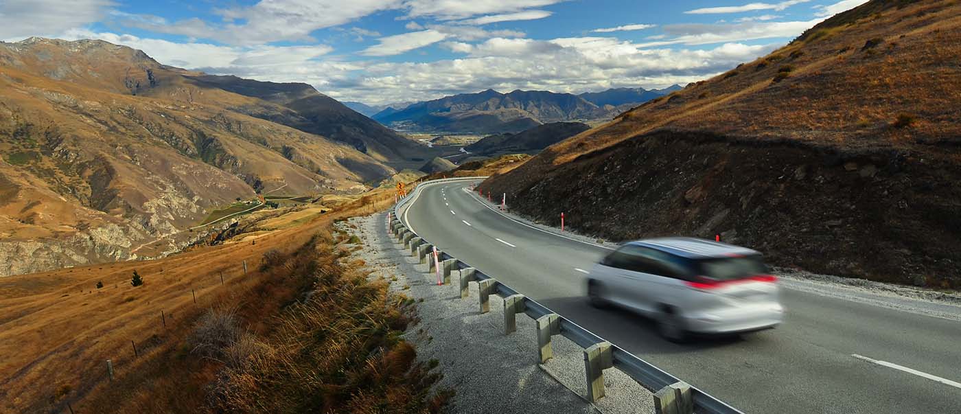 An SUV driving on the road to Queenstown, New Zealand from the east, surrounded by mountains. An SUV driving on the road to Queenstown, New Zealand from the east, surrounded by mountains.