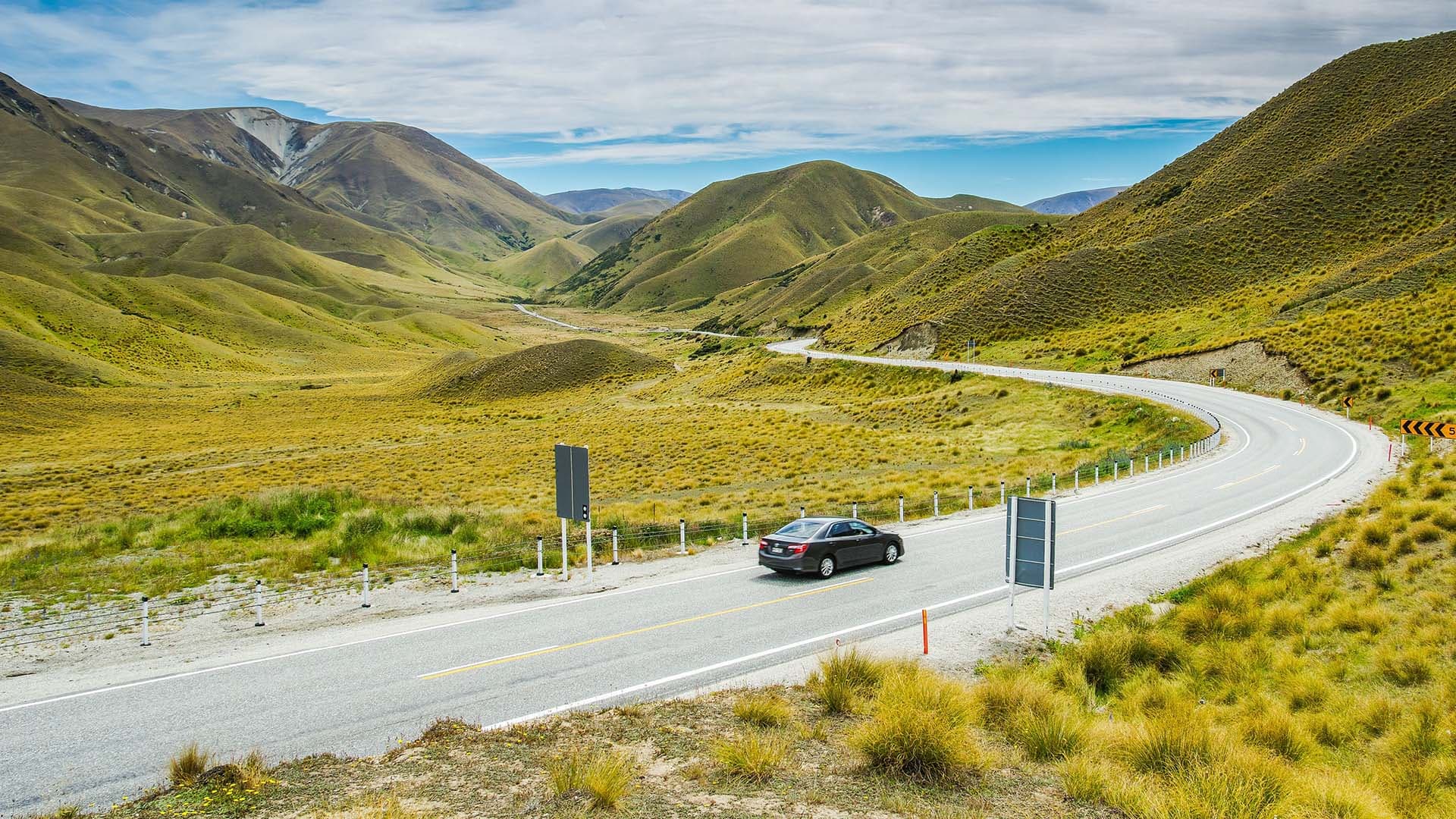 A beautiful view of a black car on road in the mountains in Lindis Pass New Zealand. A beautiful view of a black car on road in the mountains in Lindis Pass New Zealand.