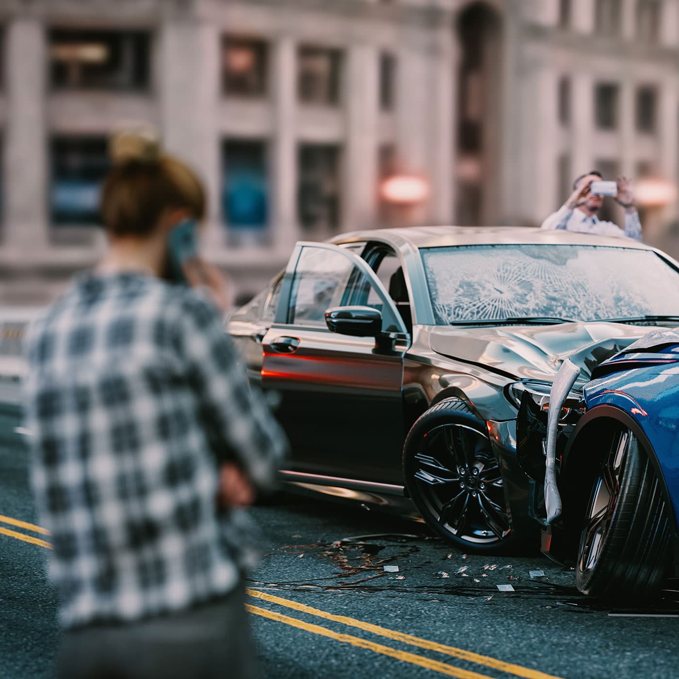 Image of a car accident with one person on the phone in the foreground, and another person taking a photo of the damage. Image of a car accident with one person on the phone in the foreground, and another person taking a photo of the damage.