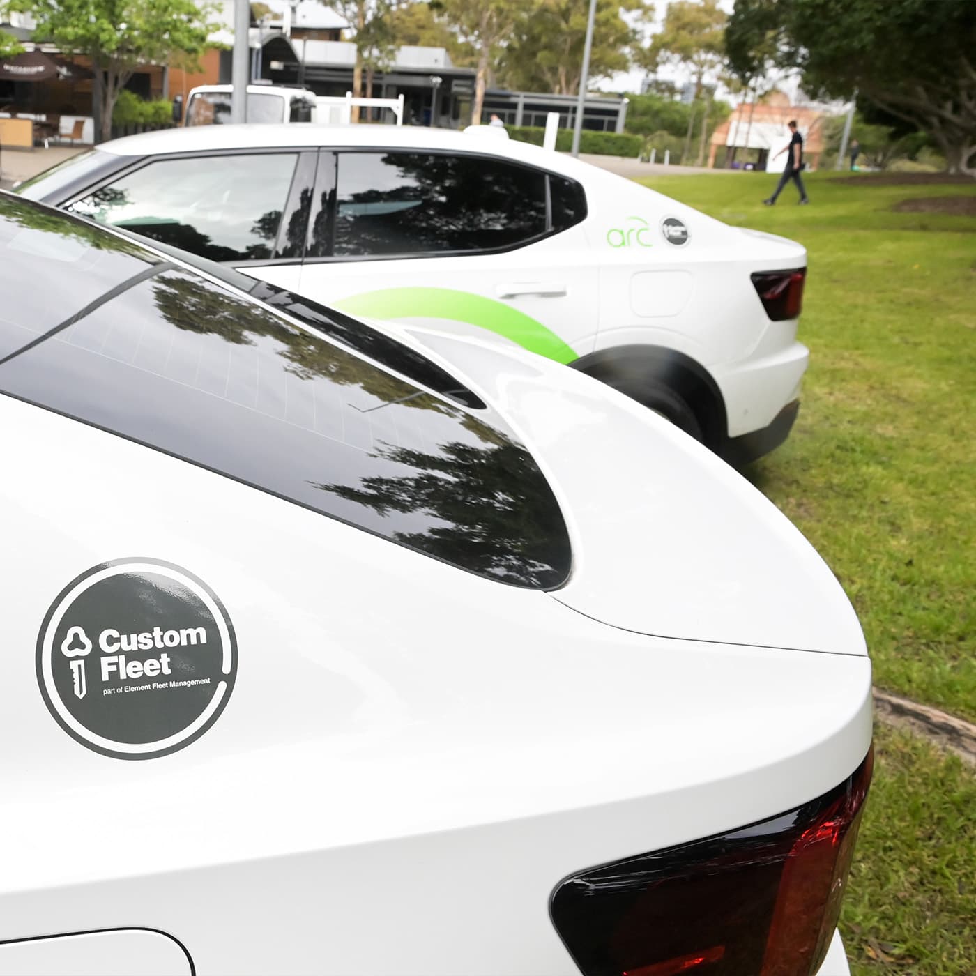 A close up photo of the back-end of two white EVs with the Custom Fleet logo on them, parked outside. A close up photo of the back-end of two white EVs with the Custom Fleet logo on them, parked outside.