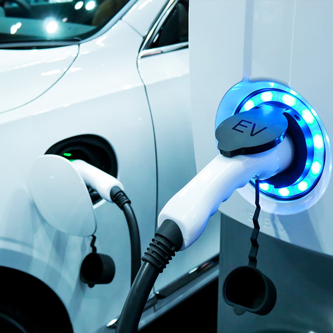 A close up of a white electric vehicle plugged in to a charging station. A close up of a white electric vehicle plugged in to a charging station.